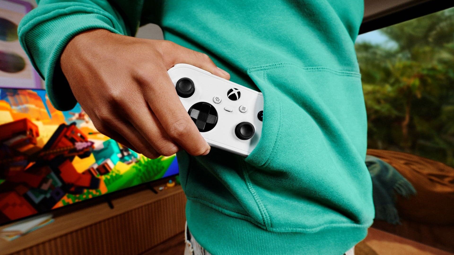 Controle Xbox Nano branco saindo do bolso de um moletom verde, em frente a uma TV